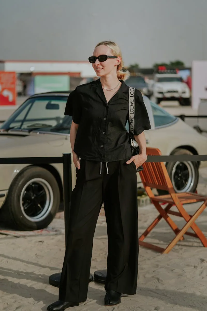 Stylish woman in black attire, standing outdoors with a vintage car backdrop, embodying modern fashion vibes in Dubai.
