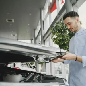 Young man checking car engine in modern dealership showroom.