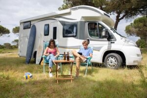 A couple enjoys a sunny day relaxing by their camper van in a picturesque outdoor setting in Portugal.