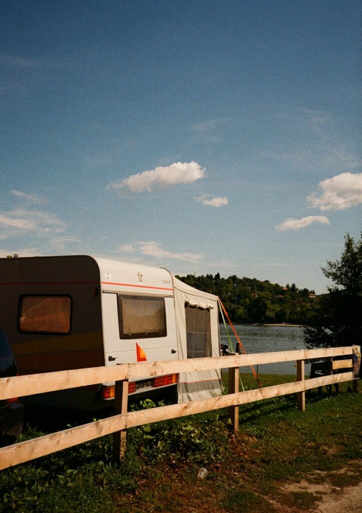 Caravan parked by a lake with wooden fence.